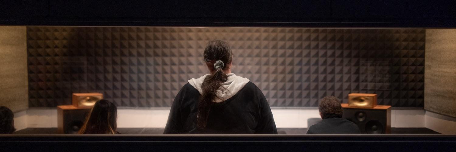 Sophie, seen from behind, in a listening room with acoustic foam and a pair of monitors